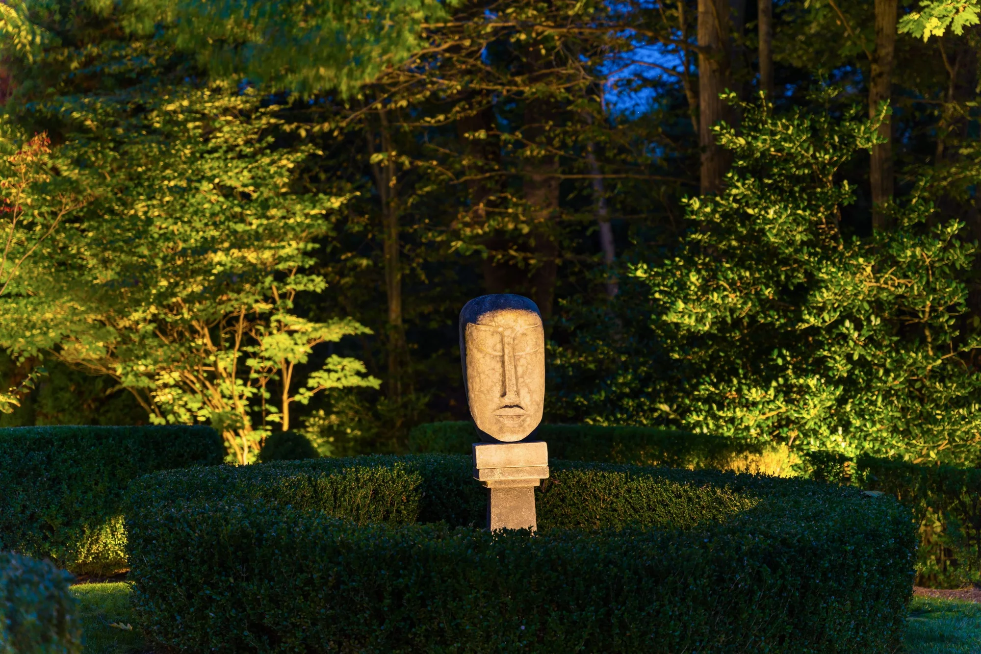A sculpture illuminated among clipped hedges and trees at Beauty in Briarcliff.