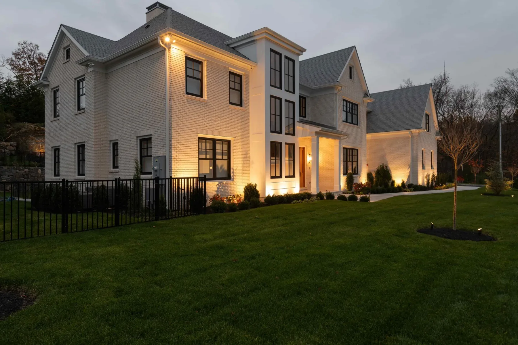 Warm lighting across a pale house exterior and shrubs along the foundation.