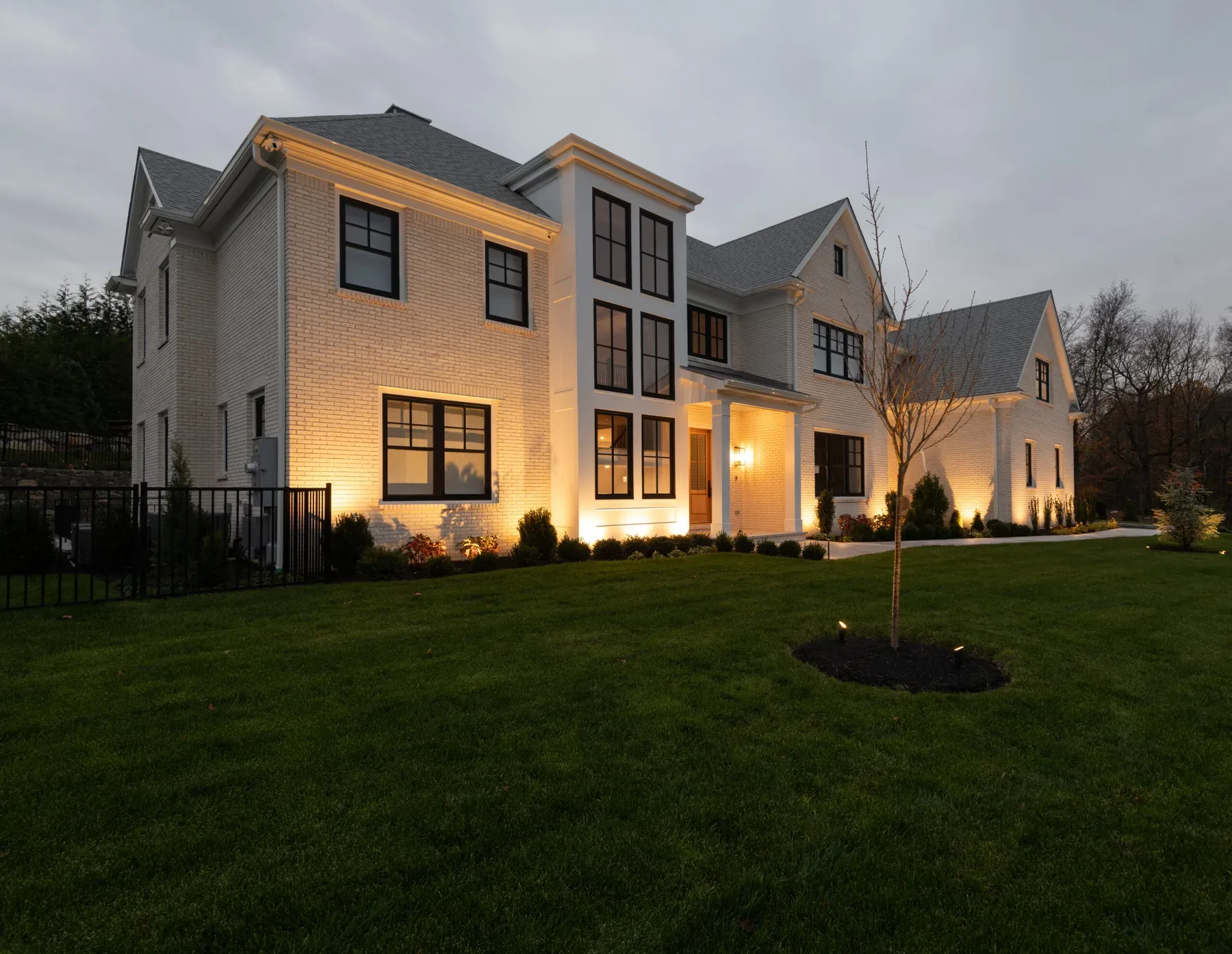 Warm lighting across a pale house exterior and shrubs along the foundation.