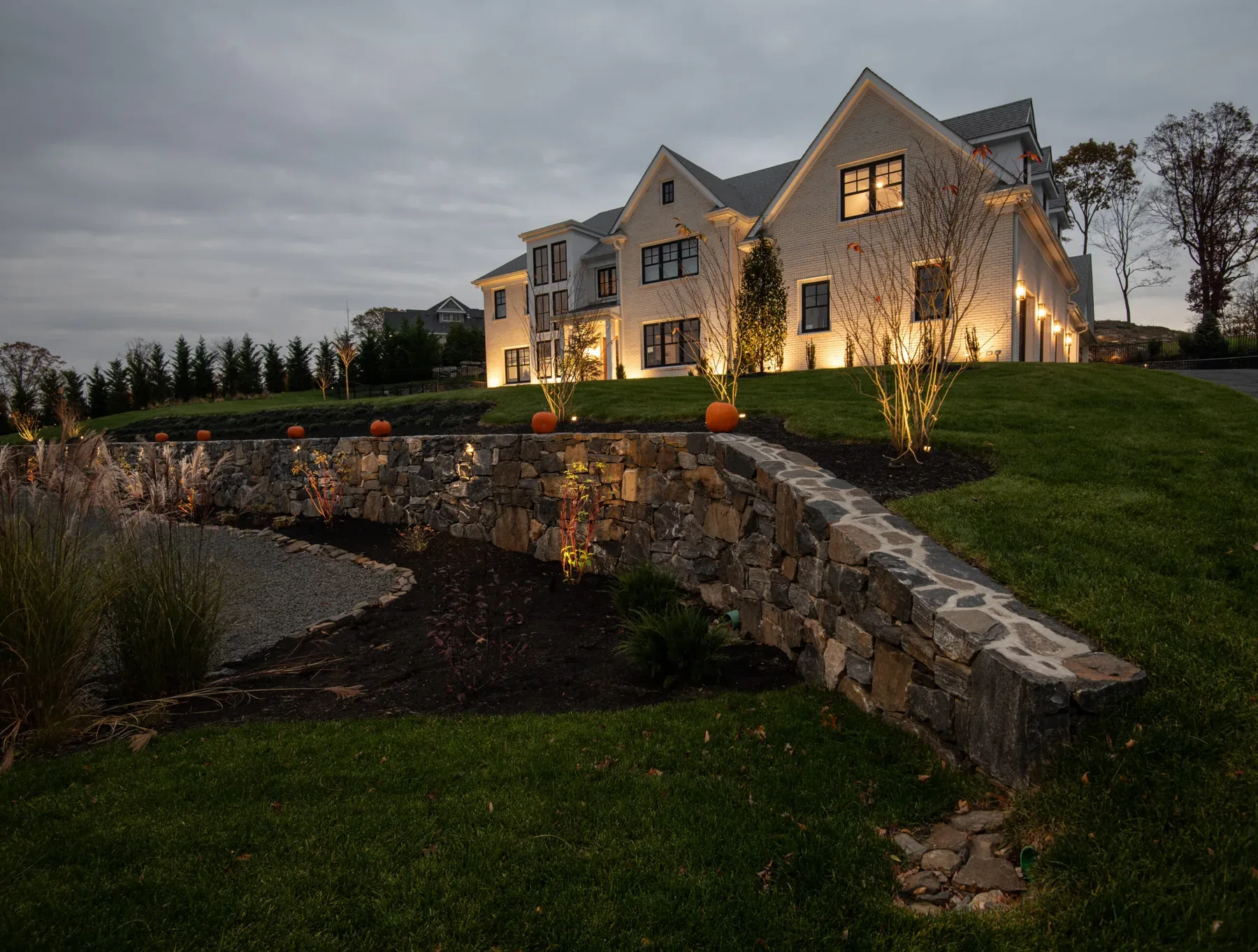 Illuminated house on a sloping lawn above a curved stone wall.