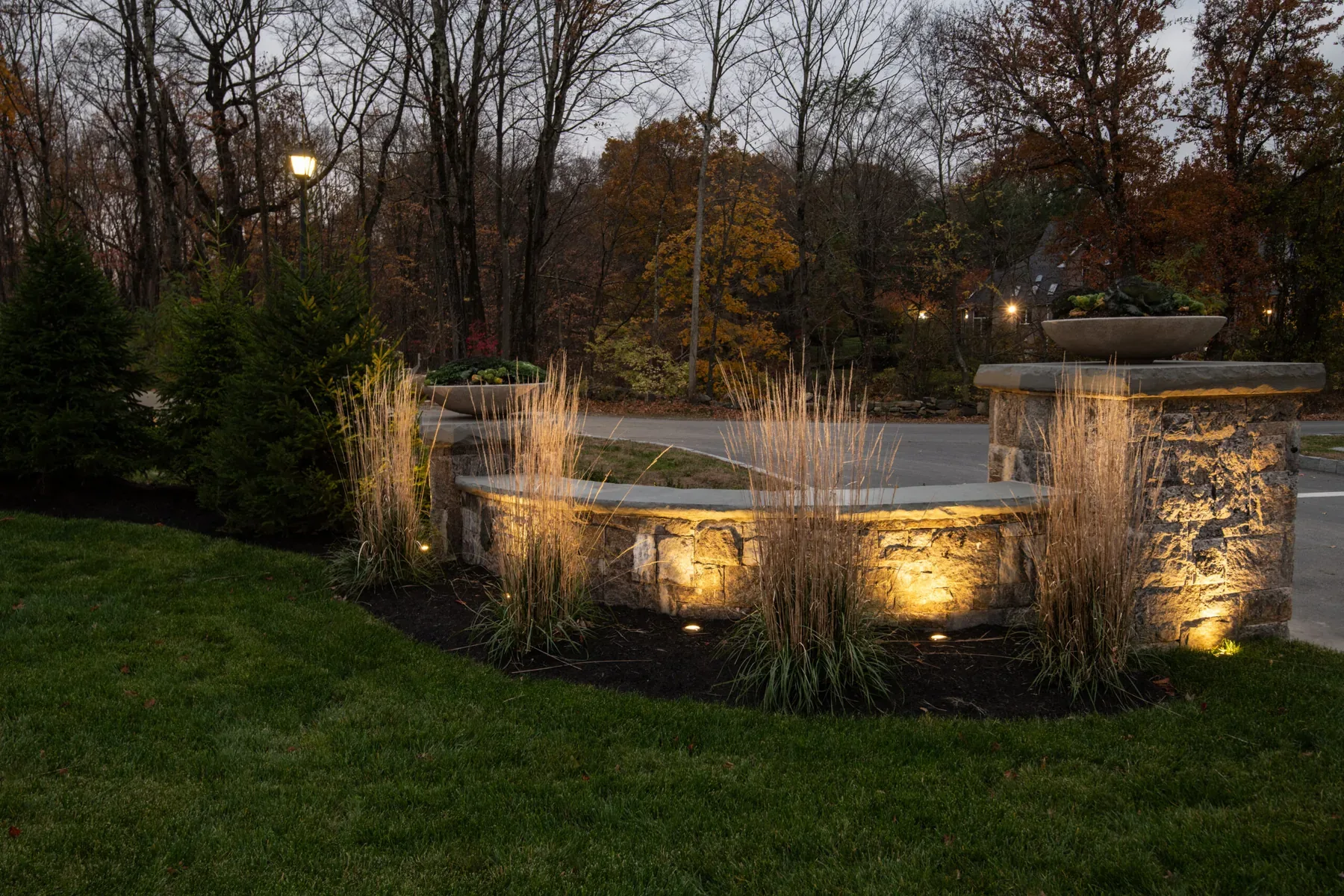 Lighting on a low stone entrance wall, pillars, and ornamental grasses.