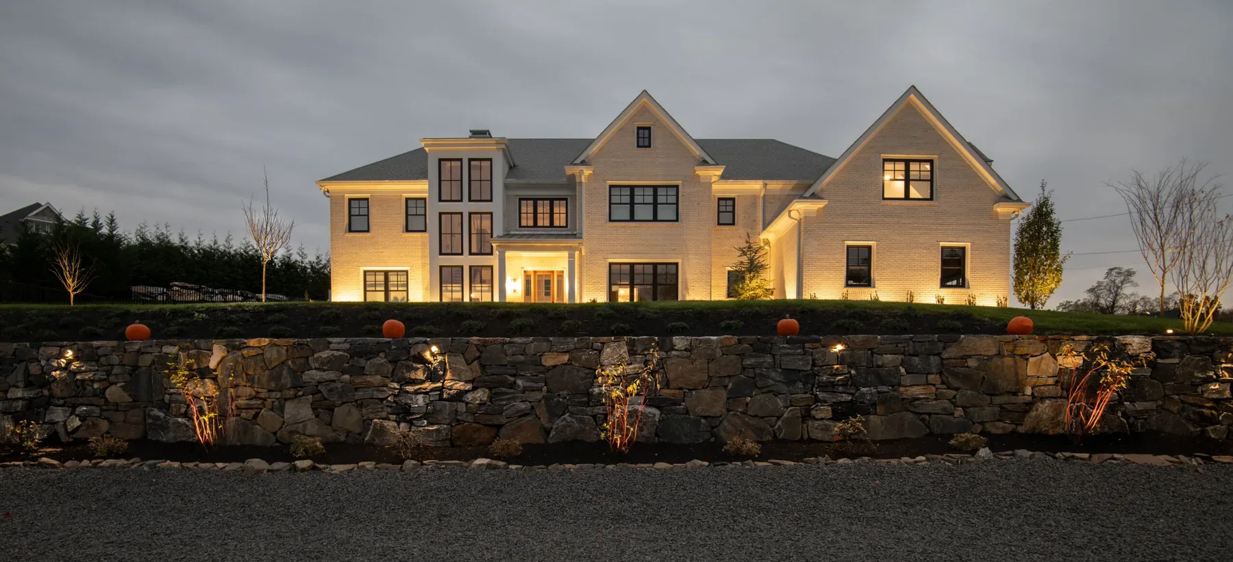 House facade and long stone retaining wall illuminated at dusk.