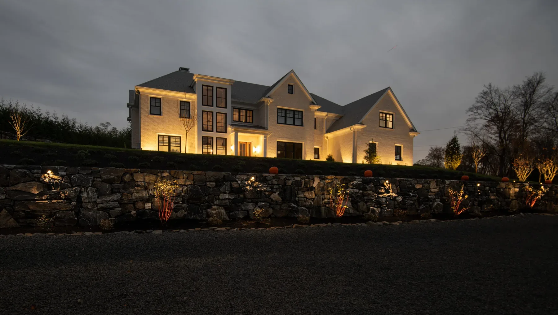 House facade and long stone retaining wall illuminated at dusk.