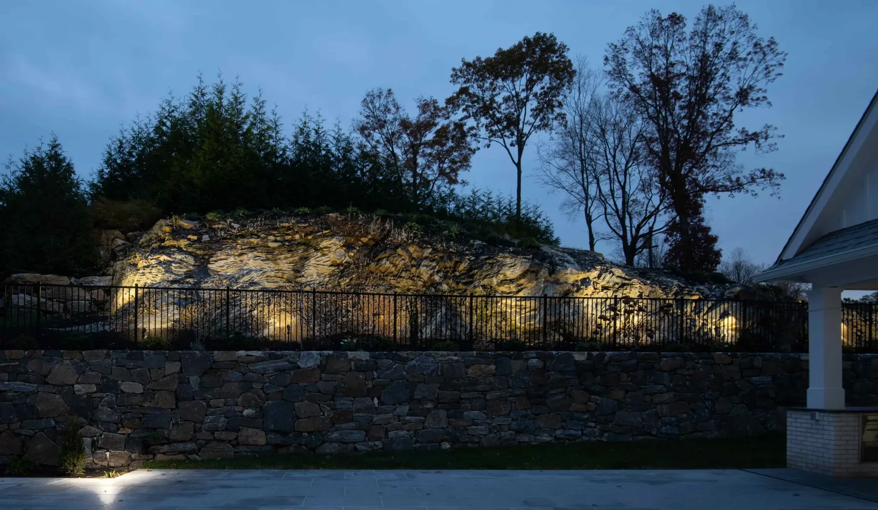 Natural rock outcrop illuminated above a dark stone retaining wall.