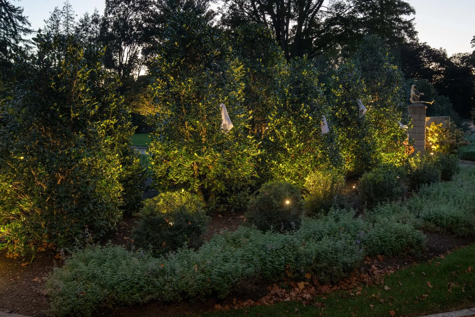 Low garden lights among shrubs beside a stone entrance pillar.