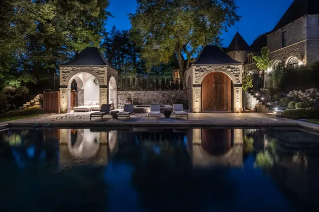 Stone pool house and surrounding trees reflected in a swimming pool at night.