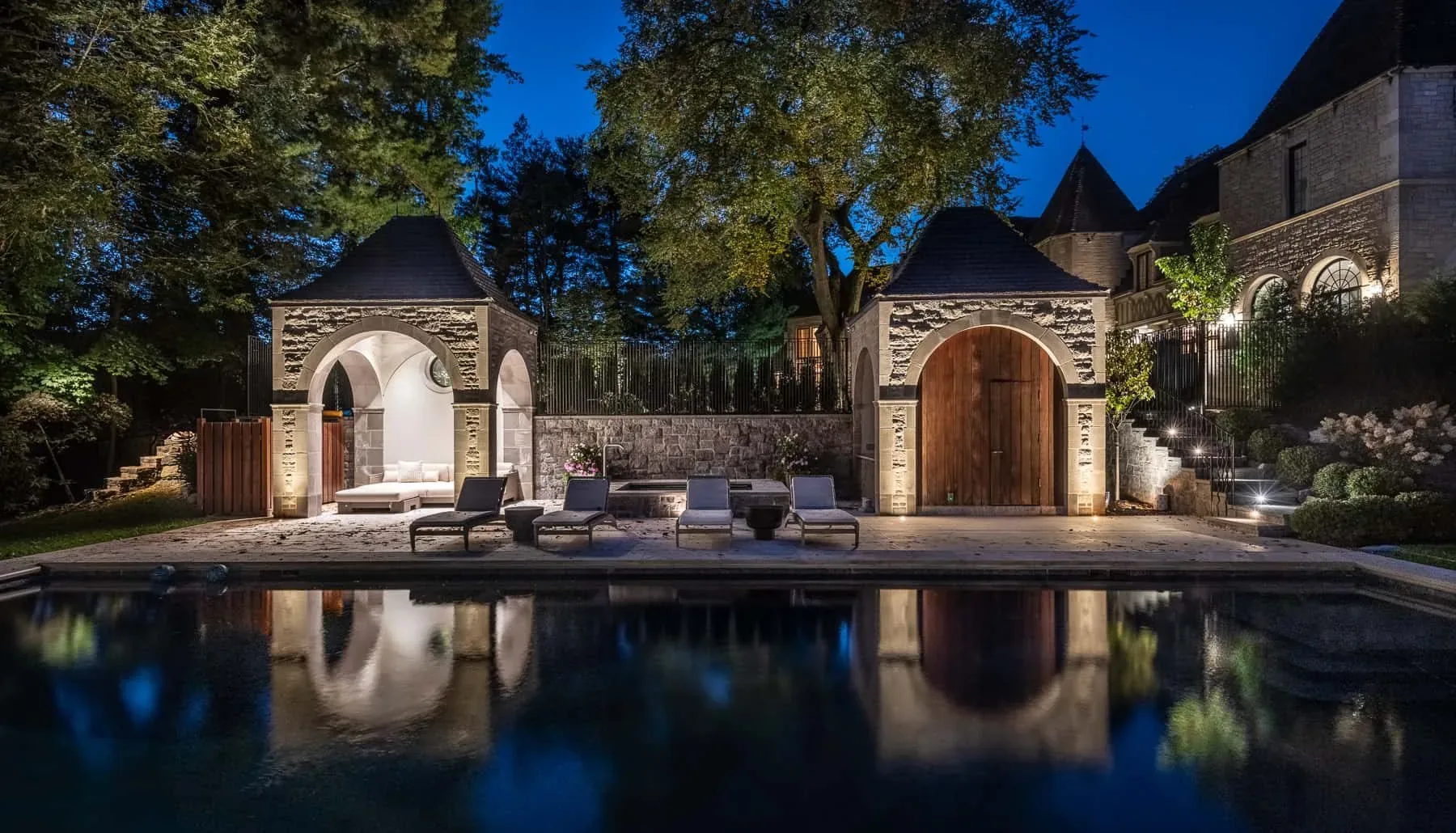 Stone pool house and surrounding trees reflected in a swimming pool at night.
