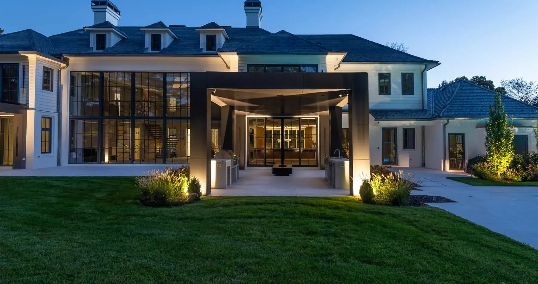 Illuminated glass entrance and white house exterior at dusk.
