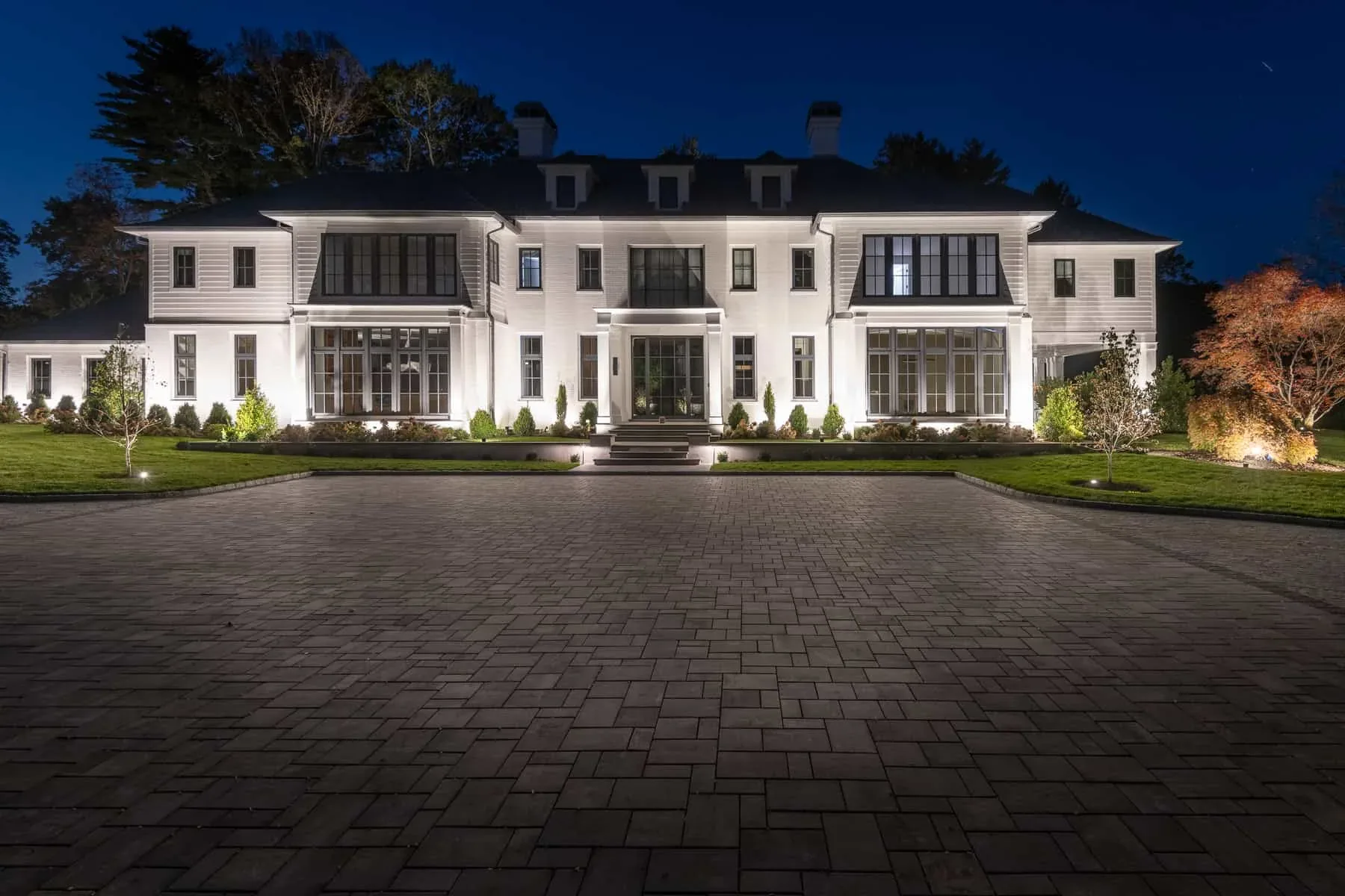 Illuminated front facade and entrance viewed across a cobblestone driveway.