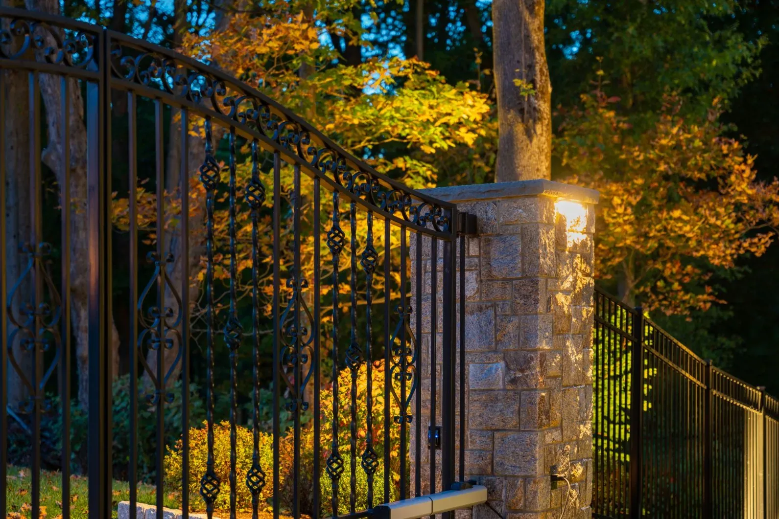 Light on a stone gate pillar beside a black metal entrance gate.