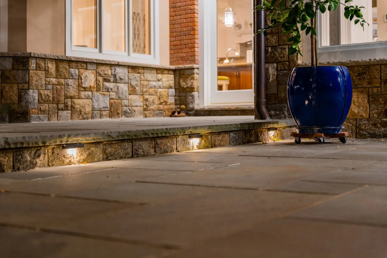 Small lights set into stone steps beside a house entrance and planter.