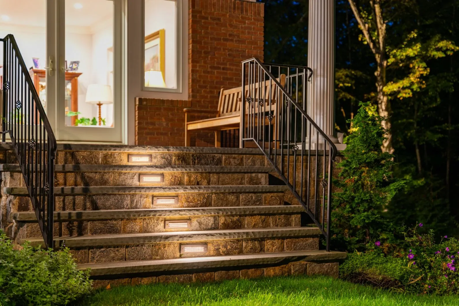 Lights along stone stairs leading to a porch with black railings.