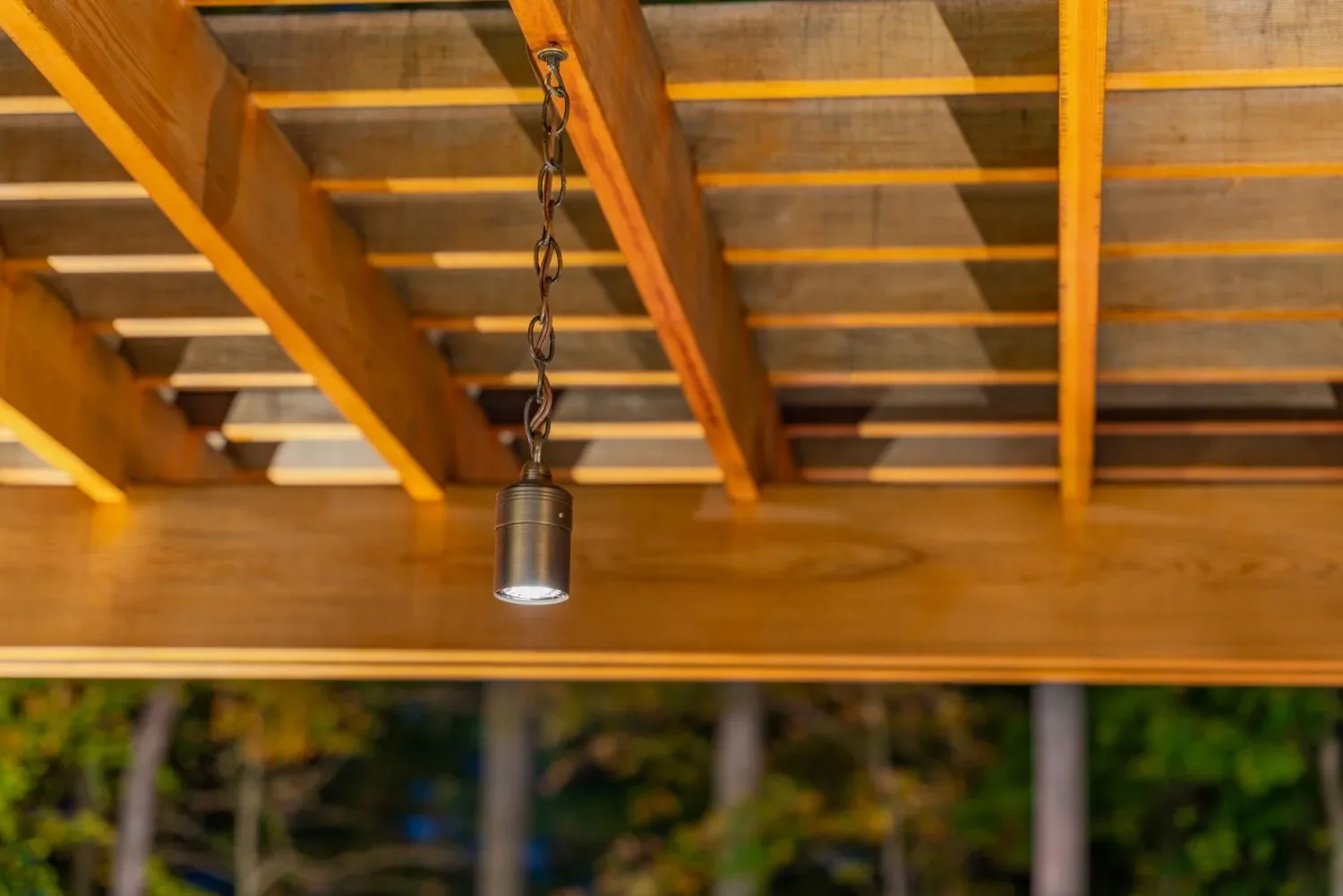 Small cylindrical downlight mounted beneath a wooden pergola beam.