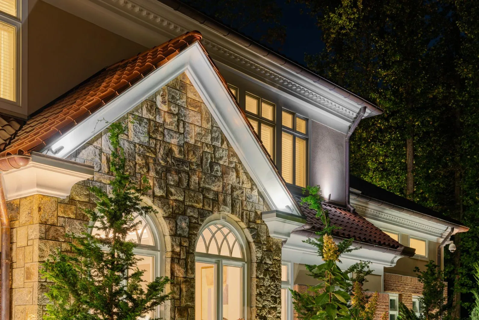 White trim and stone facade of a house illuminated at night.
