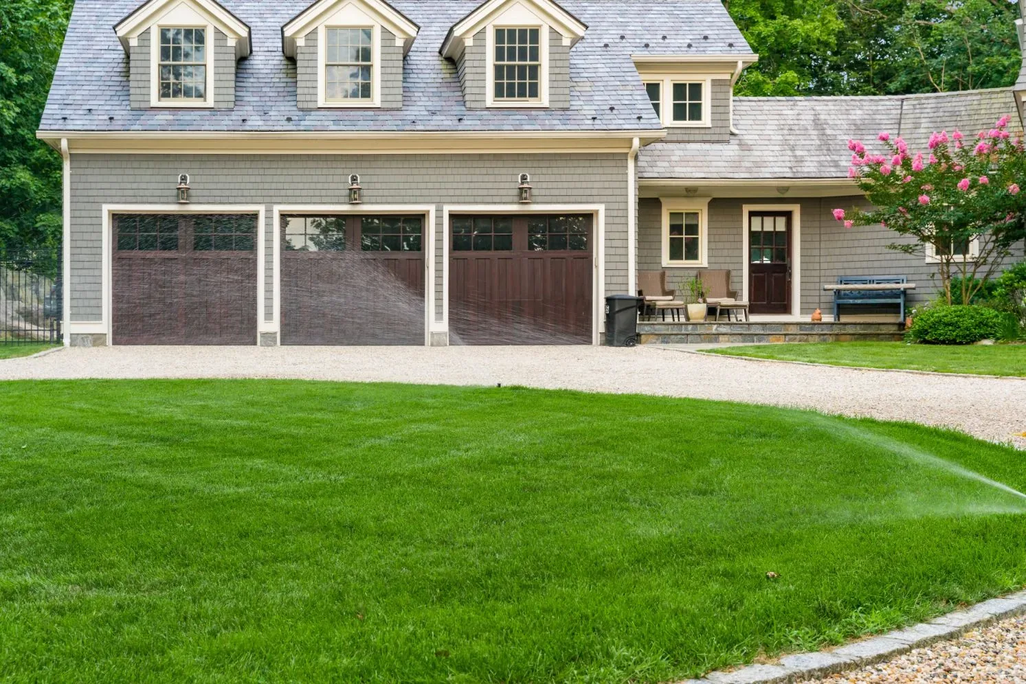 Sprinkler watering the lawn beside a garage and curved gravel driveway.