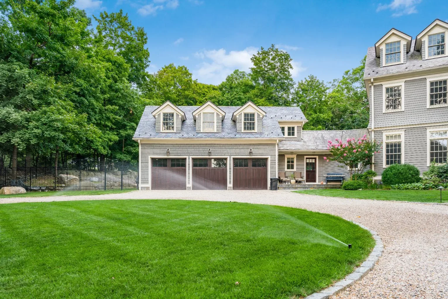 Sprinkler watering the lawn beside a garage and curved gravel driveway.