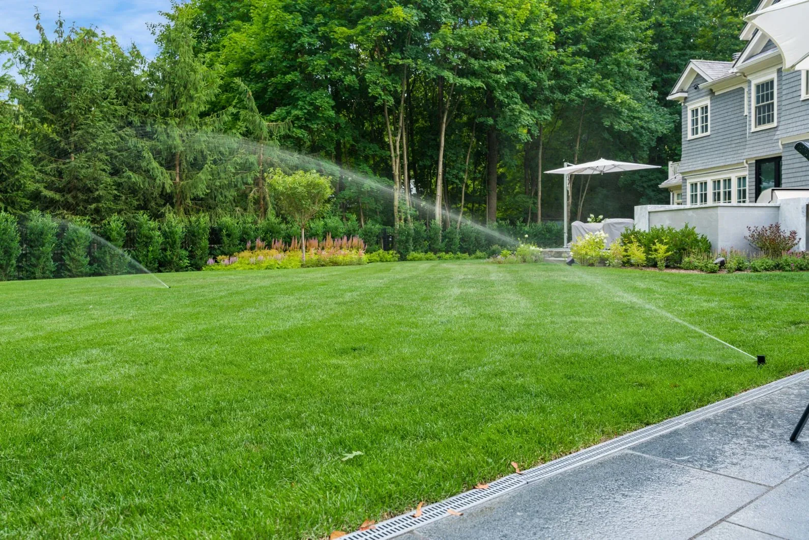 Sprinklers watering a backyard lawn beside a house and planted border.