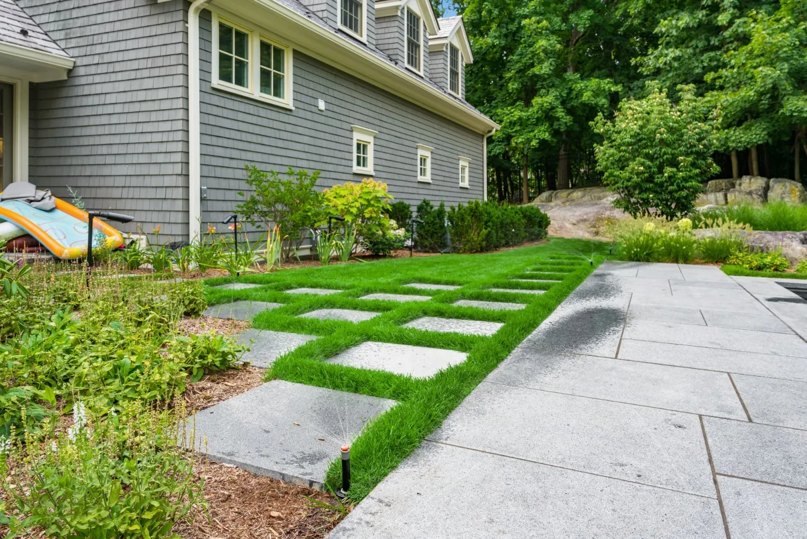 Stone pavers set in grass along the side of a gray house.