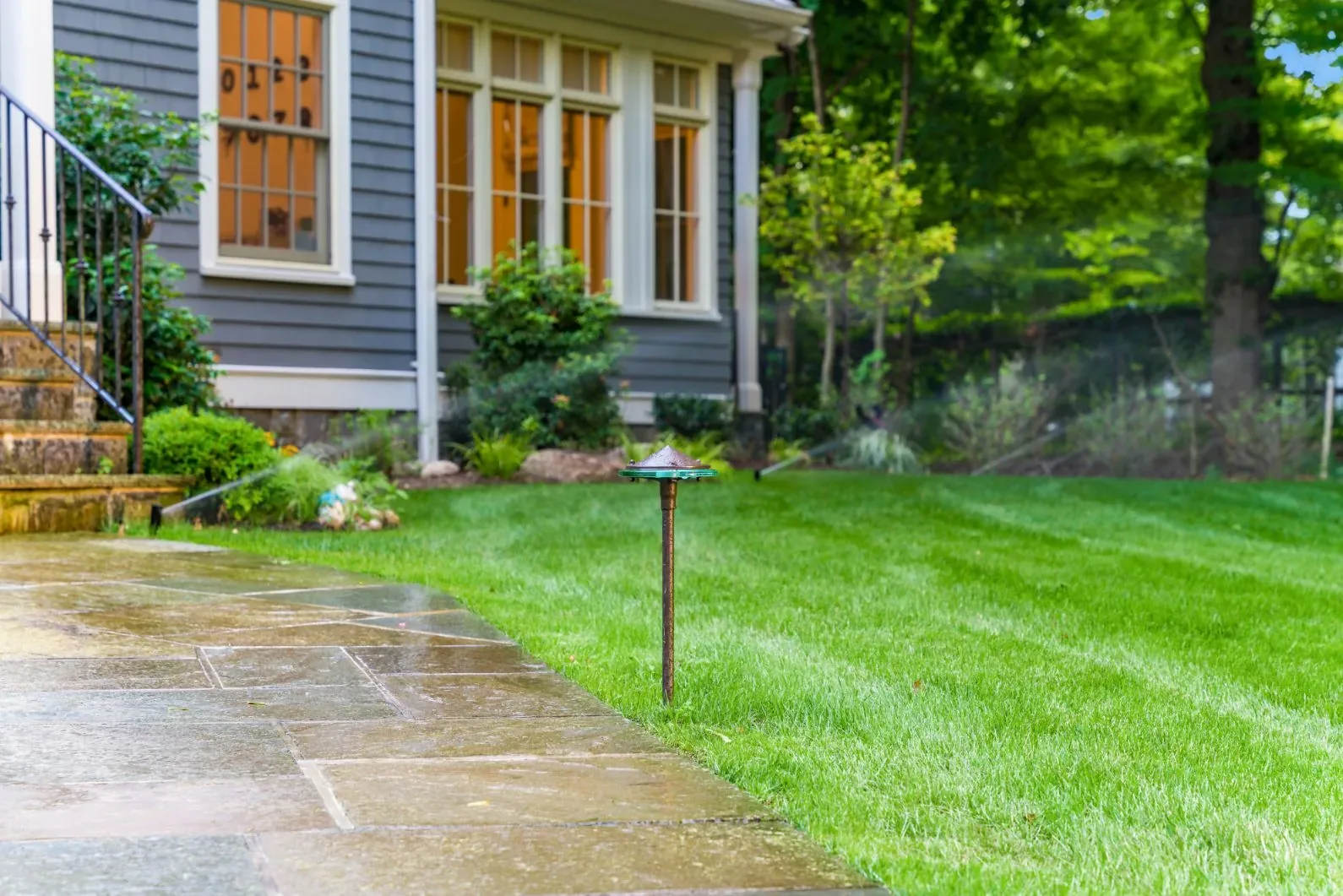 Sprinkler spray across a lawn beside a stone walkway and path light.