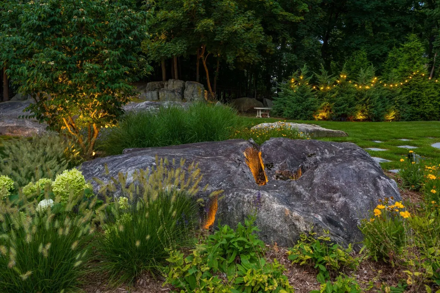 Lighting reveals the texture of a large rock among garden grasses.