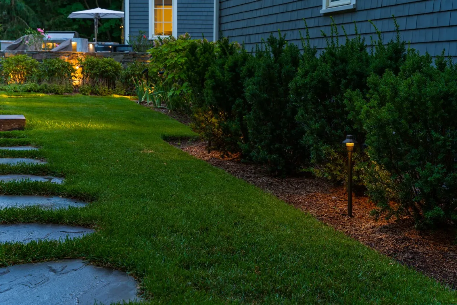 Path light beside a stepping-stone walkway and hedge at dusk.