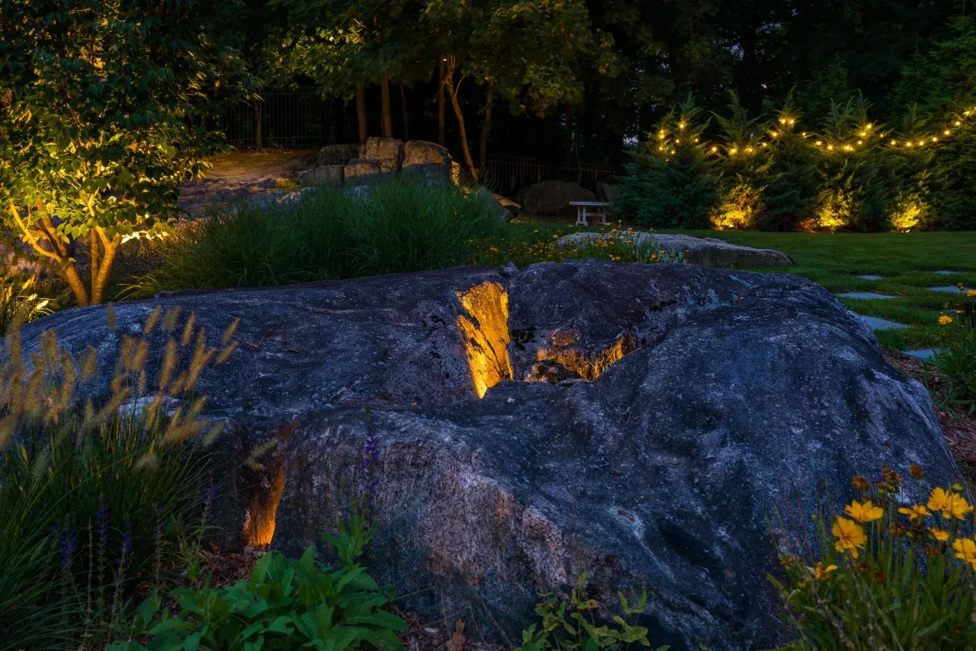 Lighting reveals the texture of a large rock among garden grasses.