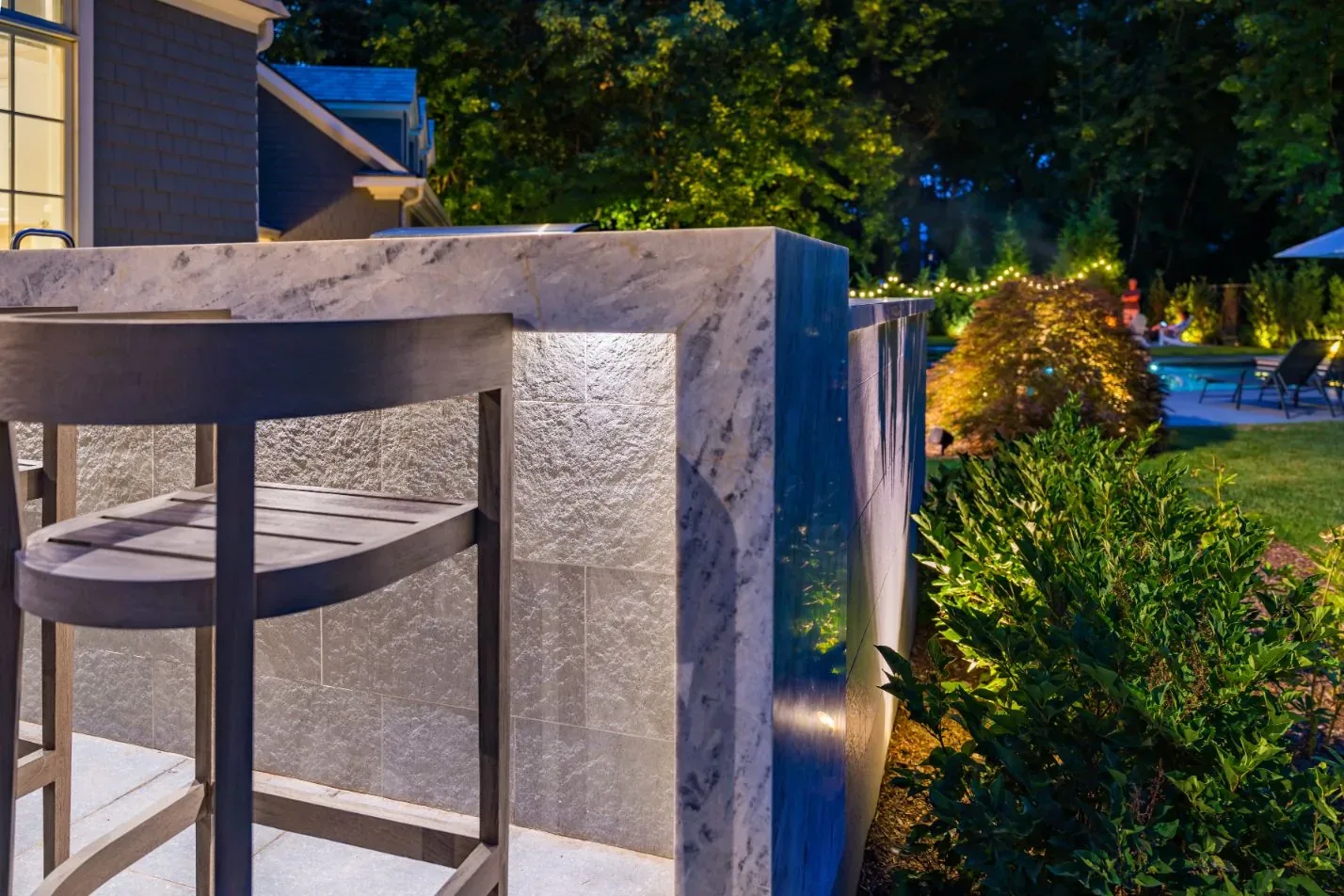 Stone outdoor bar and stools illuminated beside a house at night.