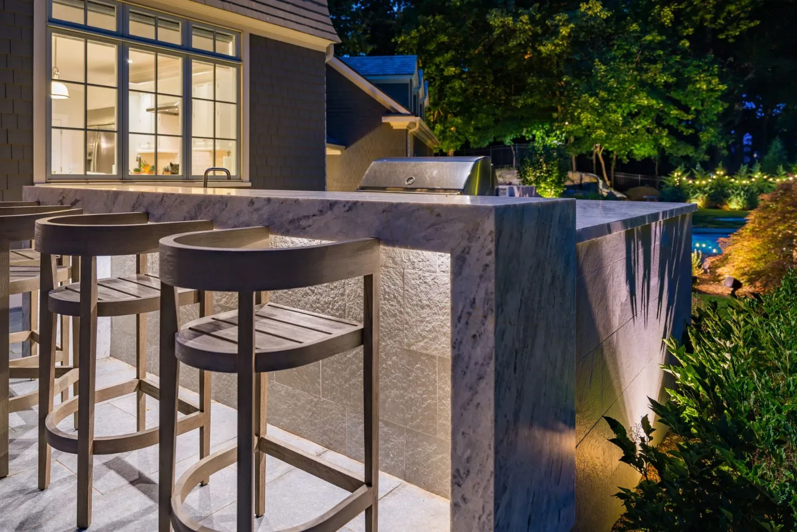Stone outdoor bar and stools illuminated beside a house at night.