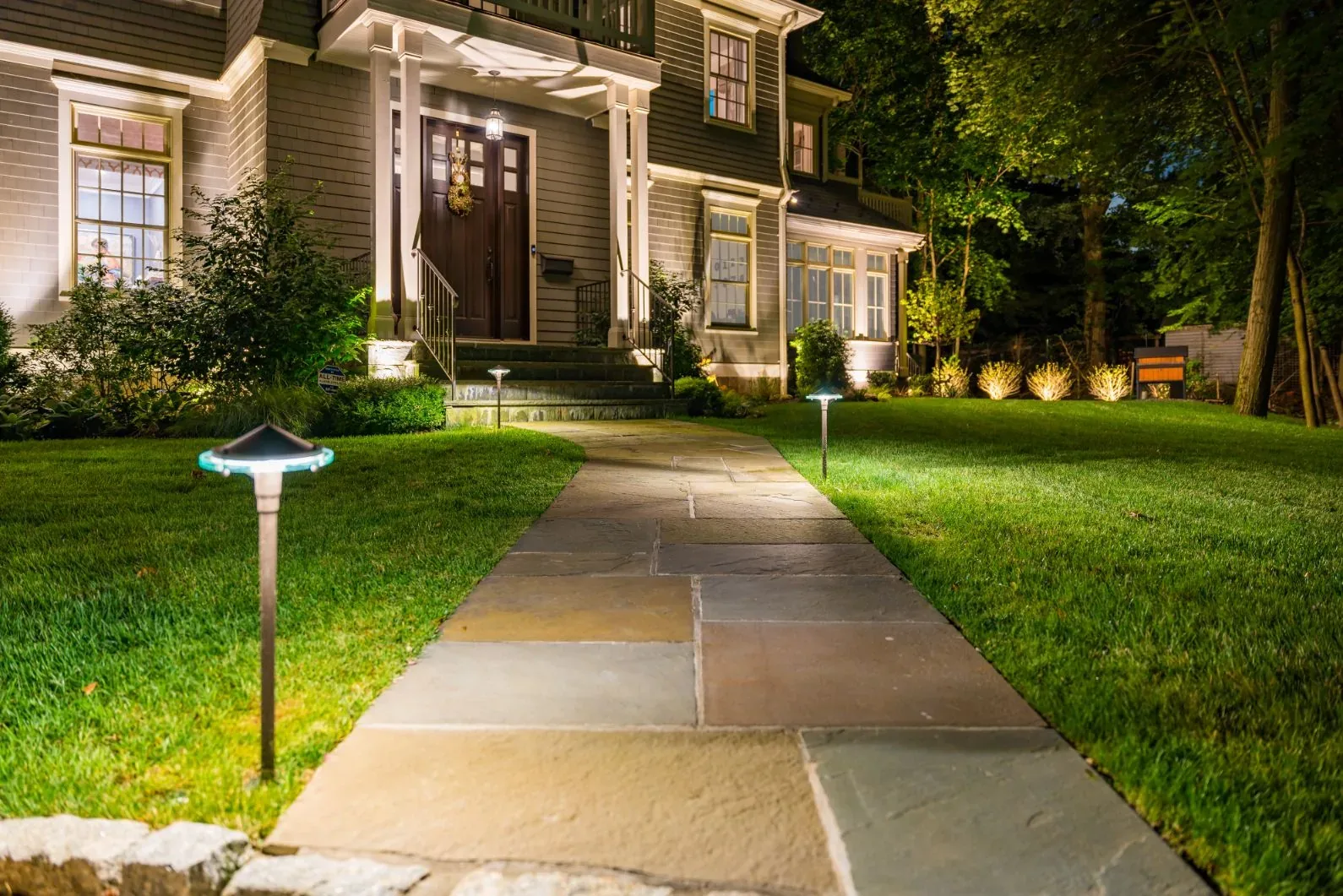 Small path lights lining a stone walkway toward an illuminated house.