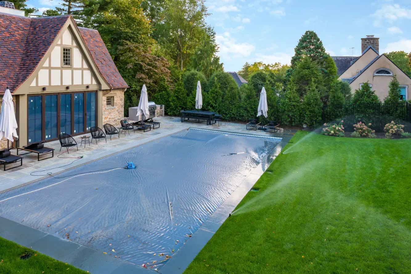 Covered swimming pool and adjacent lawn beside a stone pool house.