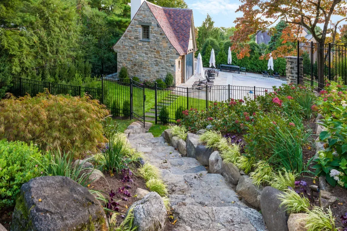 Stone garden path descending between plantings toward a fenced pool area.