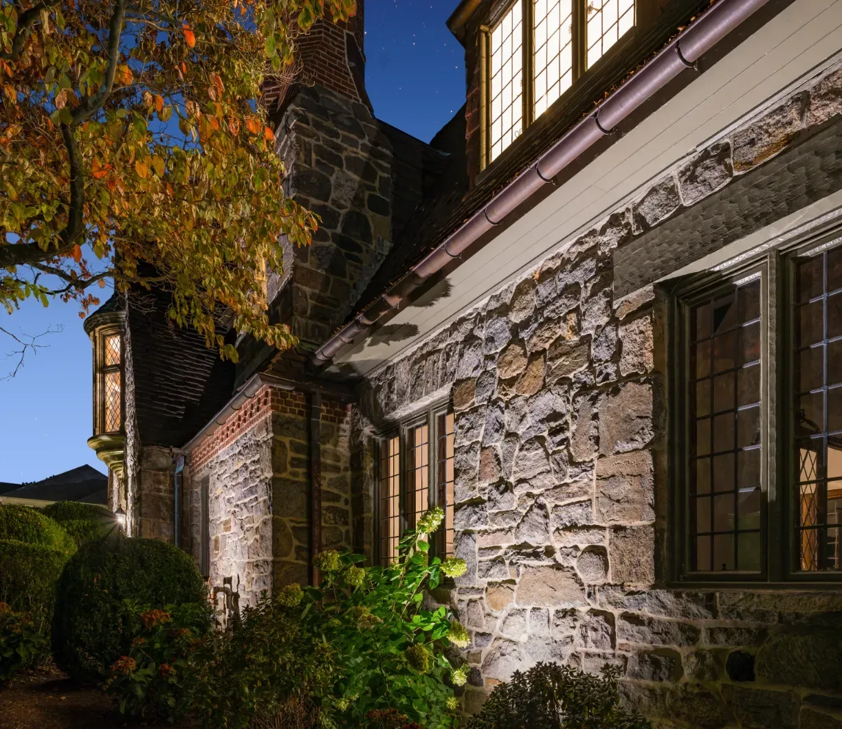 Close view of an illuminated stone house facade and garden plants.