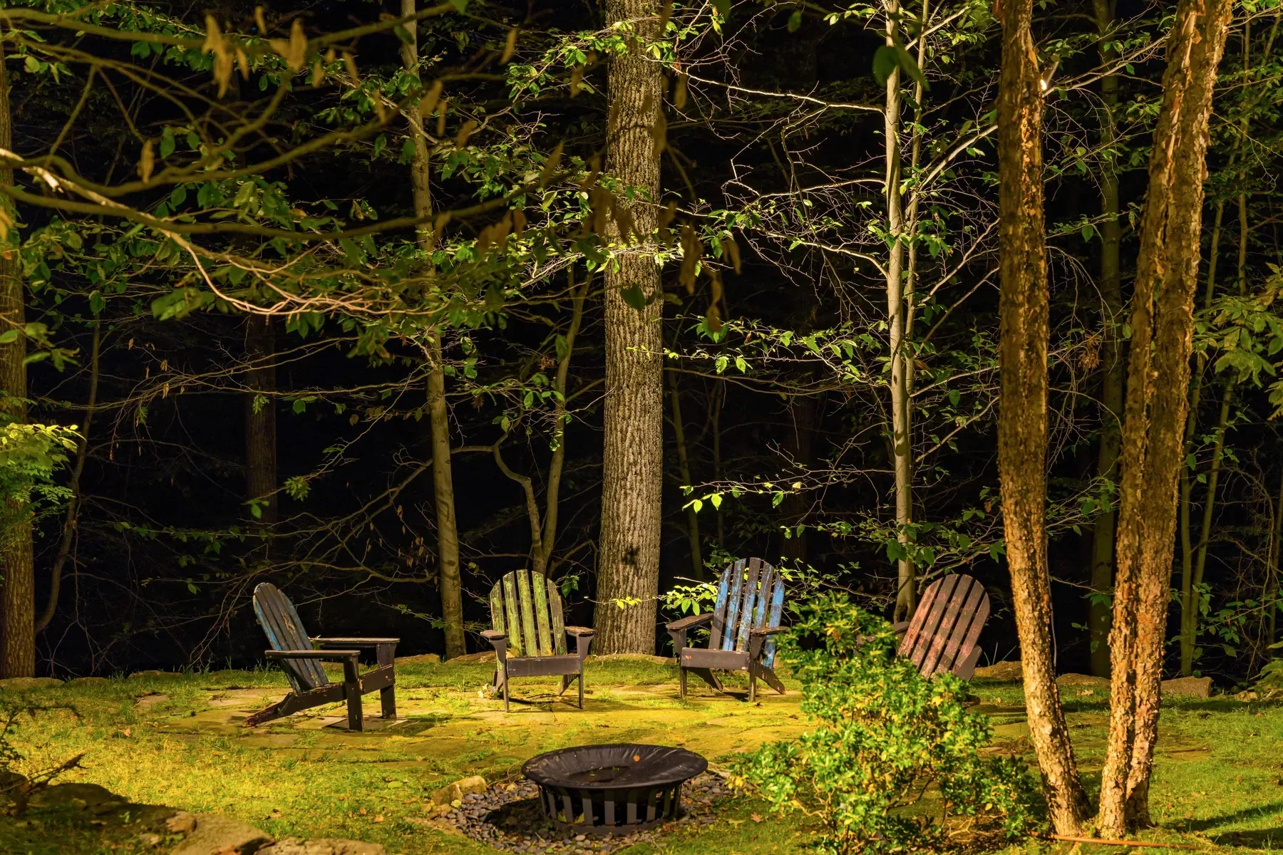 Woodland chairs and a fire pit surrounded by illuminated trees.