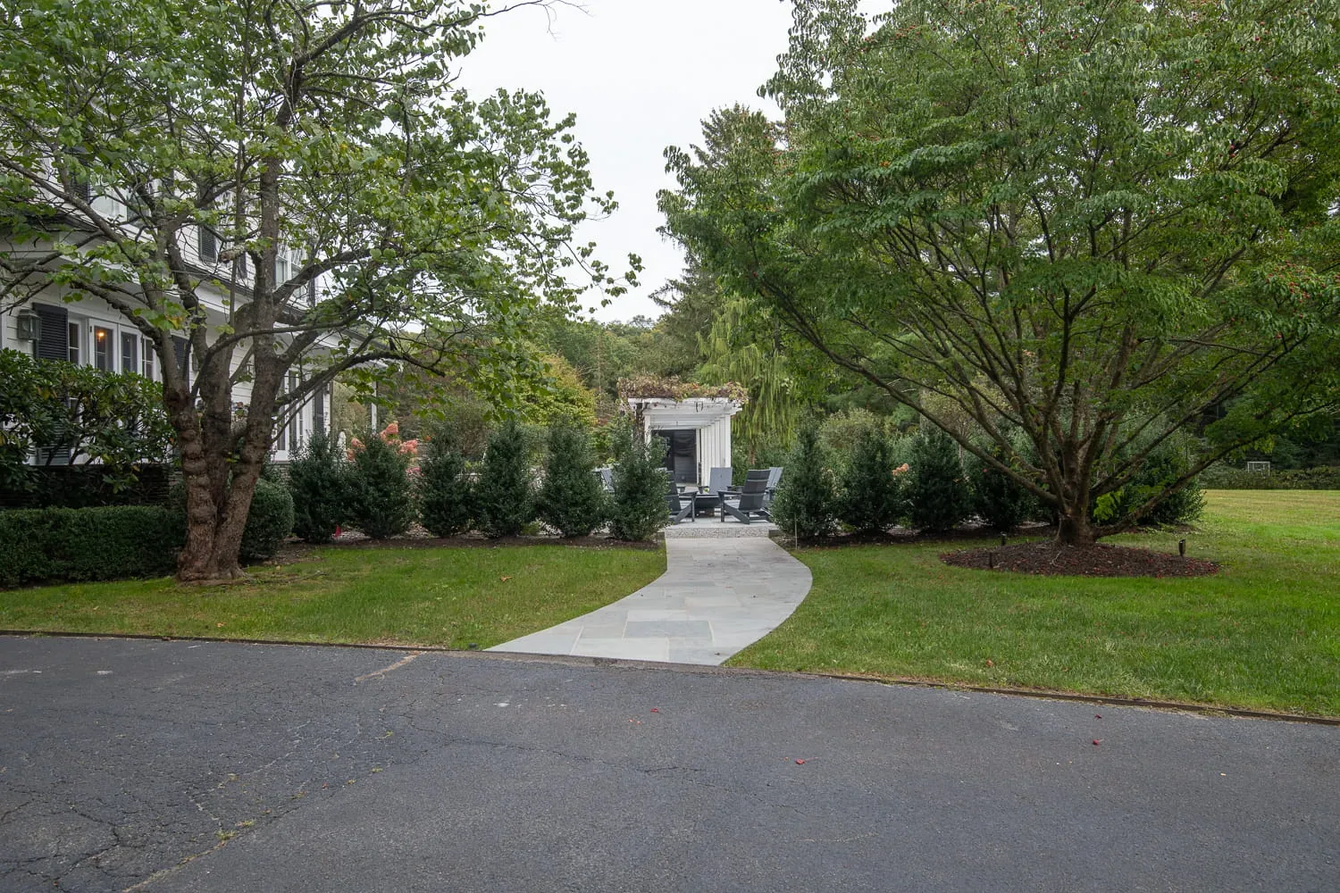 Daytime view along a curved garden path between trees and hedges.