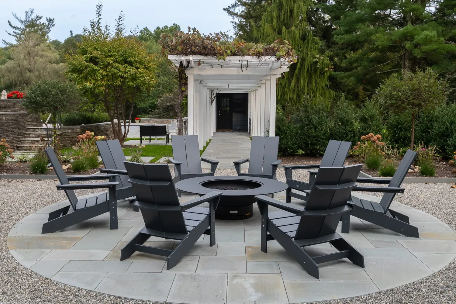 Gray chairs arranged around a circular fire pit on a garden patio.