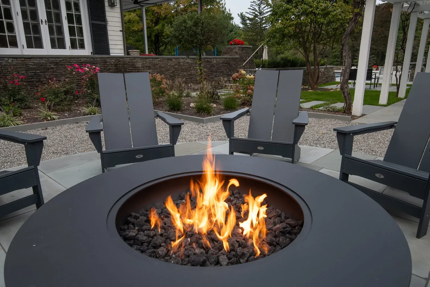Close view of flames in a round fire pit surrounded by gray chairs.