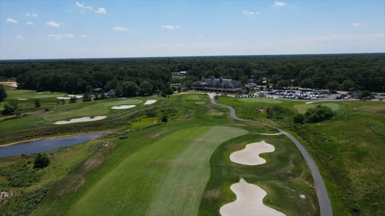 Aerial toward clubhouse; foreground fairway with right bunkers/cartpath and left pond. Original view of Scotland Run Golf Club.