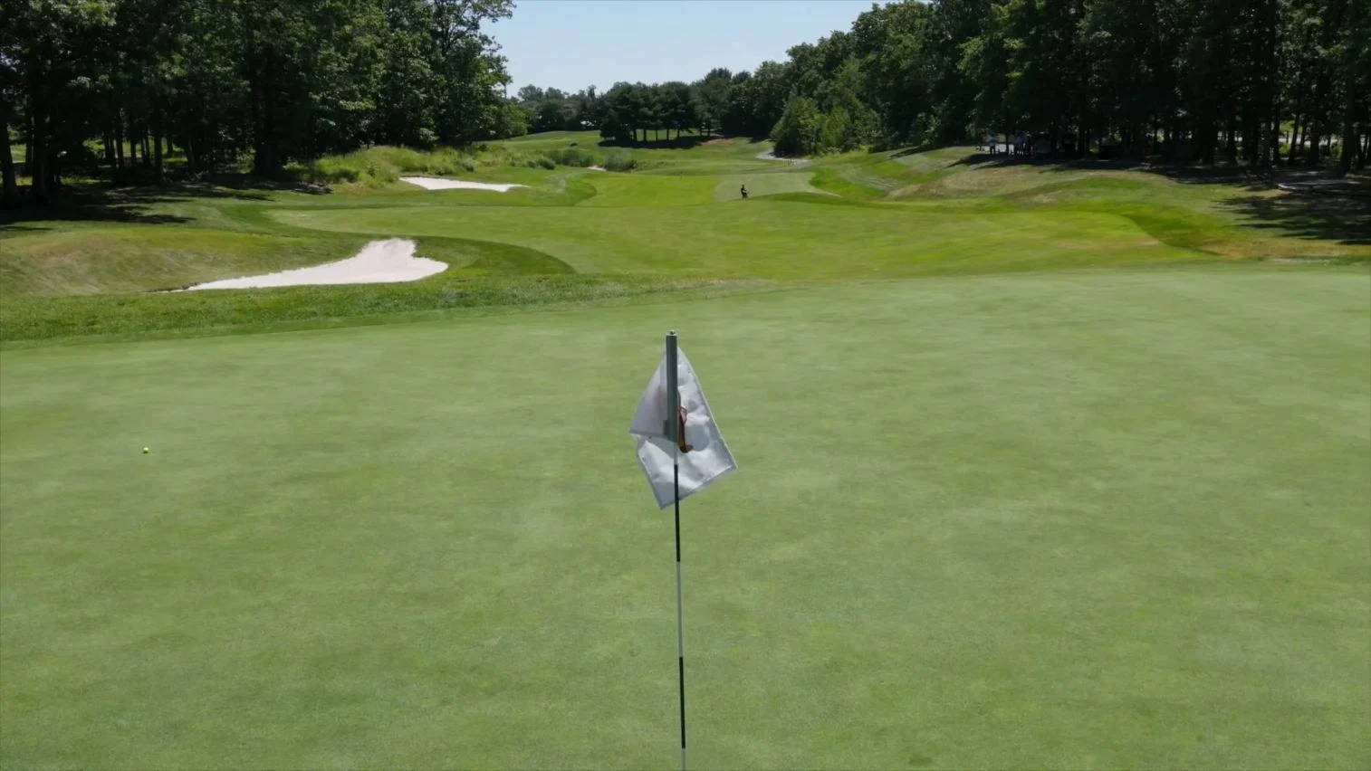 Low elevated green view with close foreground flag, two left bunkers and tree-lined fairway beyond. Original view of Scotland Run Golf Club.