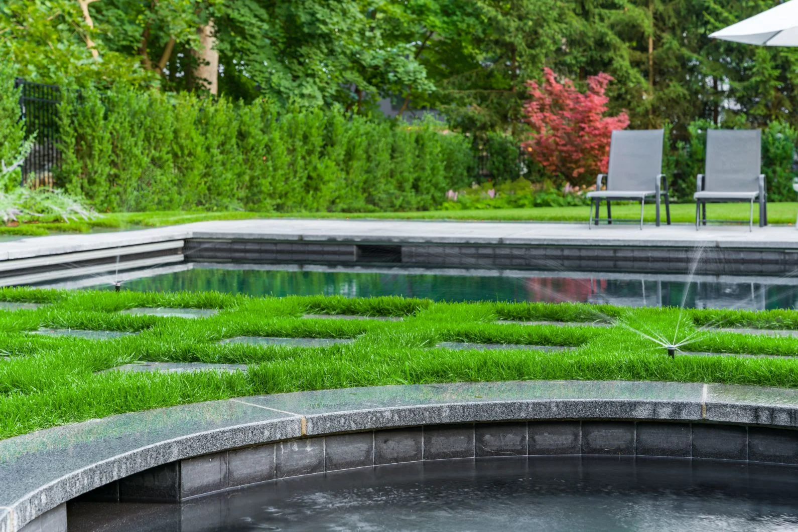 Sprinklers watering the planted areas beside the pool at Westchester Dream Home.